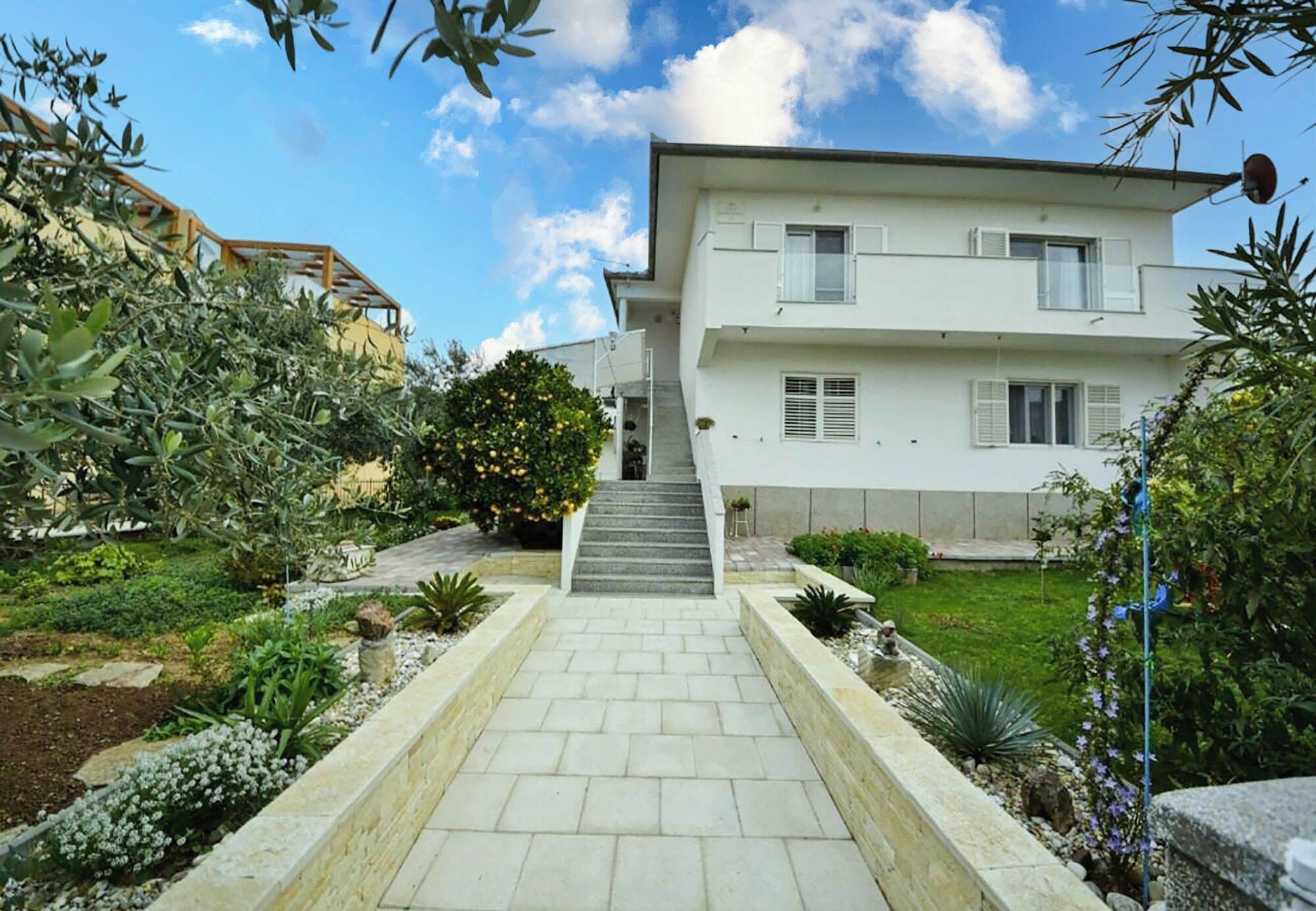 A two-story house with a paved pathway leading to the entrance.