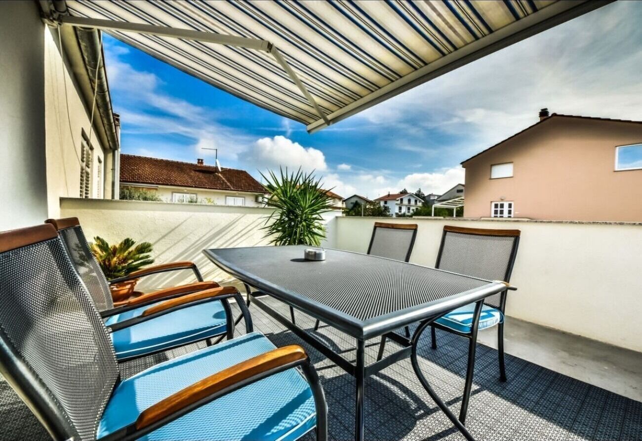 An outdoor patio with a table and chairs, a pergola, and a view of neighboring houses.