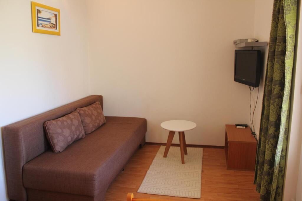 Una sala pequeña con un sofá marrón, una mesita redonda, un televisor y un altavoz.