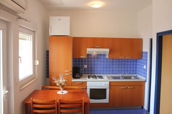 A compact kitchen with wooden cabinets, a gas stove, a sink, and a window with blinds.