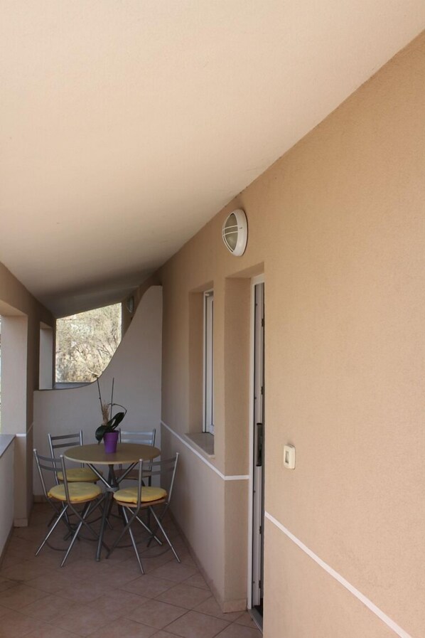 Un petit balcon avec une table et des chaises, une plante en pot et une fenêtre.