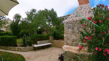 A stone-built outdoor area with a bench and a table, surrounded by greenery and a stone wall.
