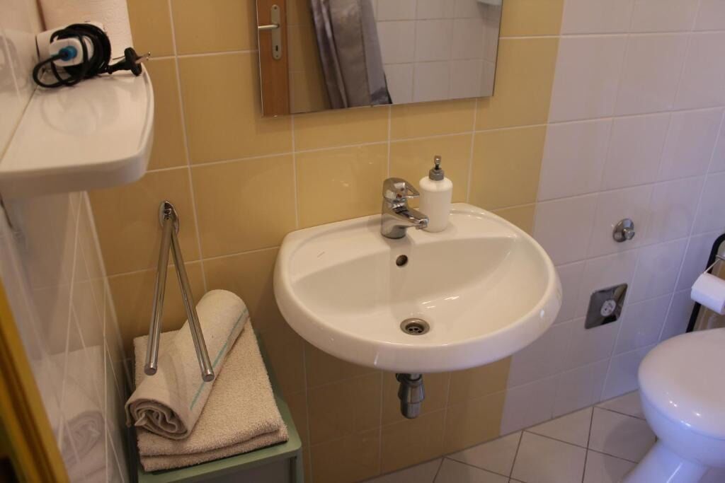 A bathroom with a white sink, a towel rack with folded towels, a mirror, and a toilet.