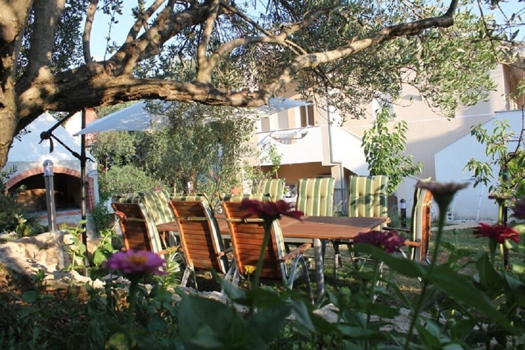 Un área de estar al aire libre con mesas y sillas de madera, rodeada de follaje y flores.
