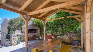 A covered outdoor area with a brick oven, a table with benches, and potted plants. - Apartments Stipe (Mali Losinj)