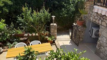 Un patio con mesa y sillas, rodeado de plantas en macetas y un muro de piedra.