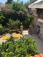 Un patio con mesa y sillas, rodeado de plantas en macetas y un muro de piedra.