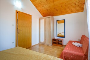 Un dormitorio con techo de madera, un armario, un espejo, una mesita de noche y una cama con cubrecama rojo.