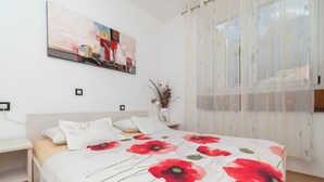 Ein Schlafzimmer mit einem Bett, einem Nachttisch, einem Wandbild und einem Fenster mit durchscheinenden Vorhängen.