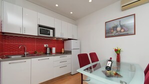 Eine moderne Küche mit weißen Schränken, einer roten Spritzschutzwand, einer Mikrowelle und einem Kühlschrank. Ein Esstisch mit roten Stühlen und eine Blumenvase stehen bereit.
