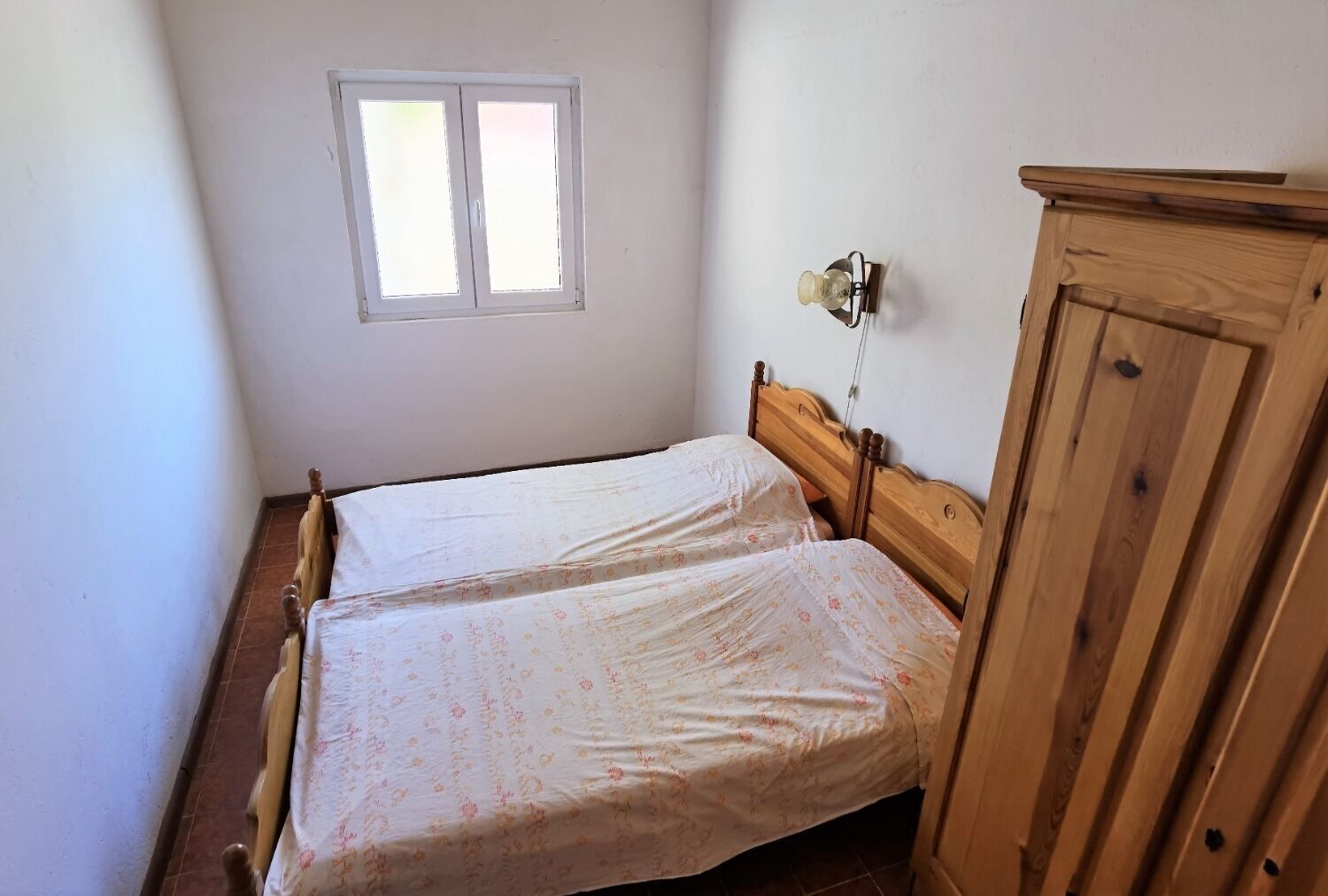 Een kleine kamer met een enkel bed, een houten hoofdeinde, een raam en een houten garderobe.