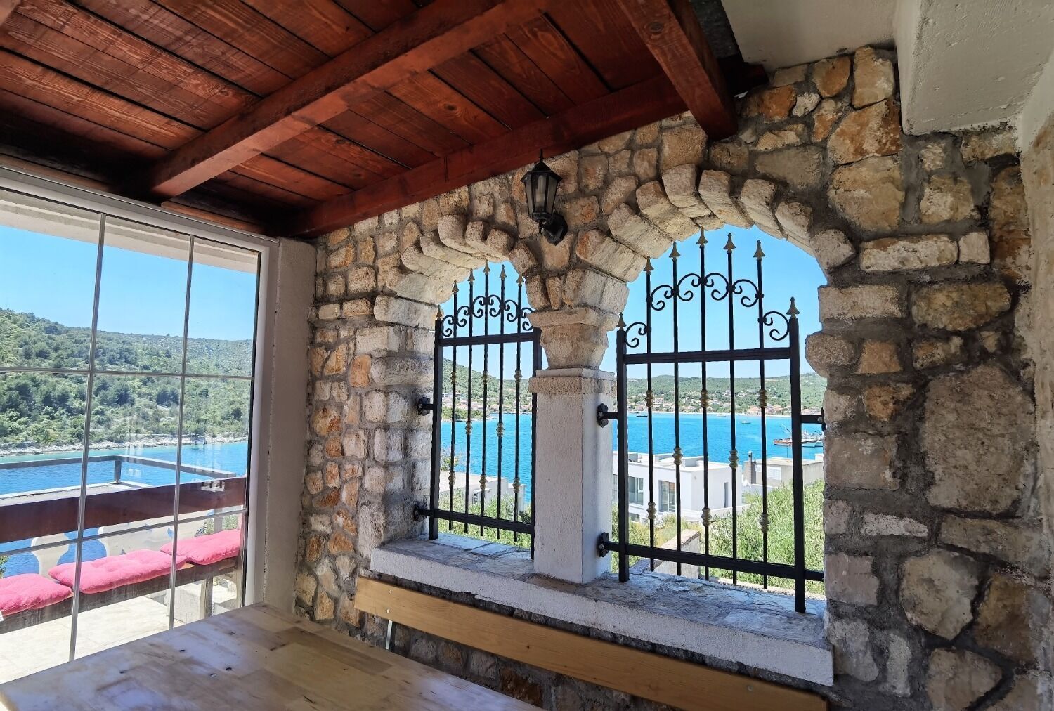 Une pièce aux murs de pierre, avec un plafond en bois, un banc et une vue sur la côte.