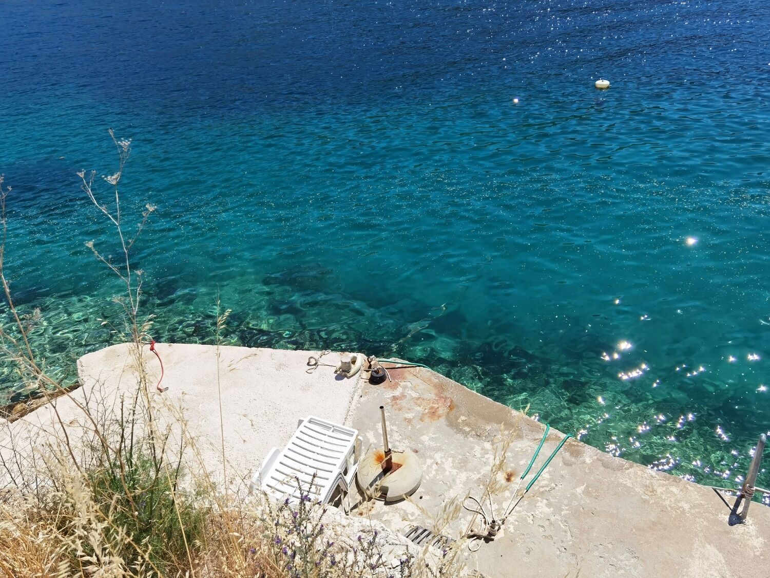 Vista despejada de una zona costera con una plataforma de hormigón, algo de vegetación y un barco amarrado cerca.