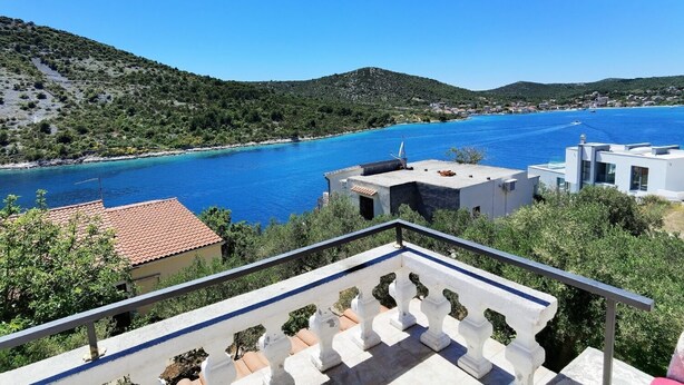 Blick auf die Küste mit blauem Meer, terrassenförmig angeordneten Häusern und einem Balkon mit Geländer.