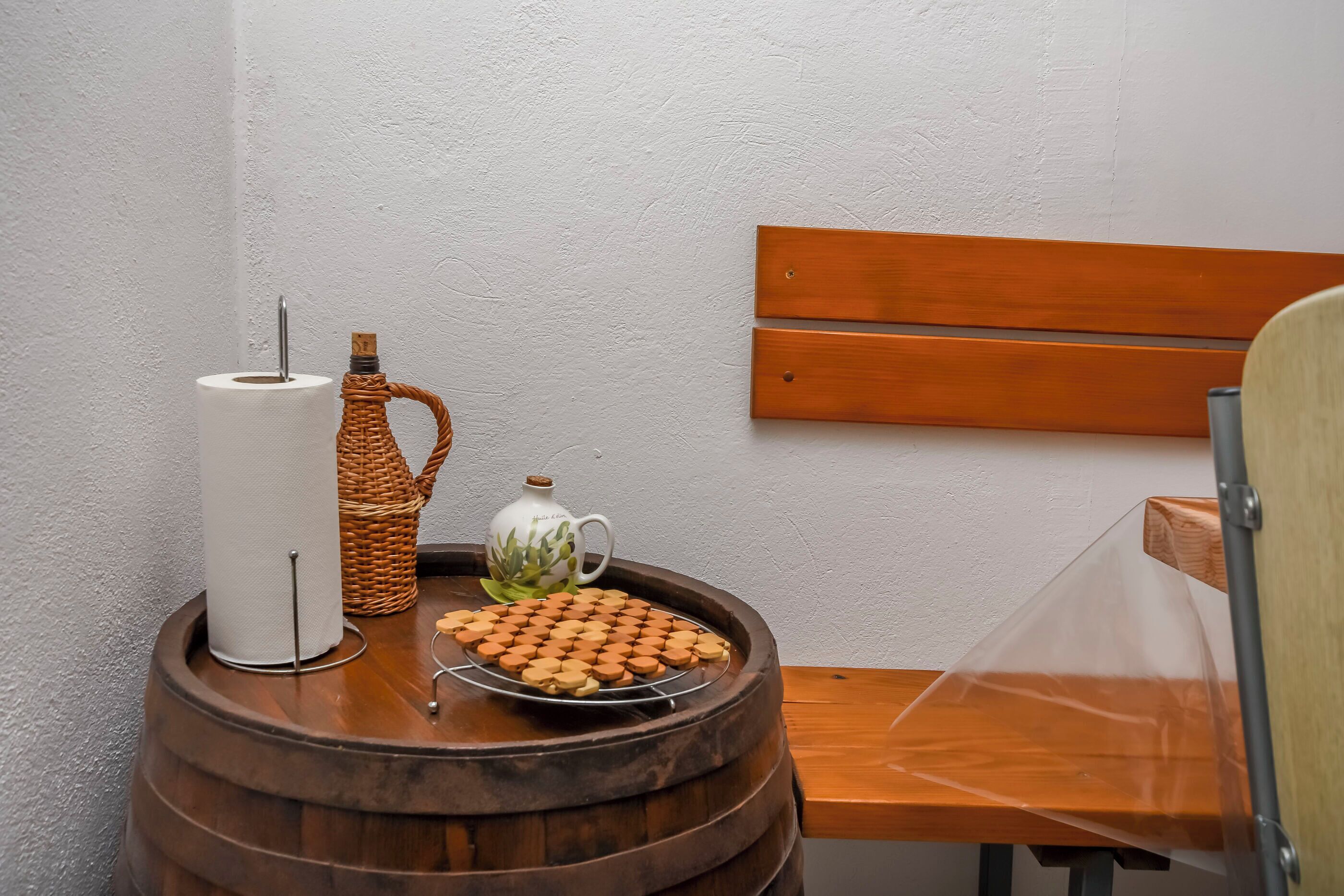 Una mesa de barril de madera con un rollo de papel higiénico, una cesta tejida, una taza de cerámica y una bandeja de galletas.