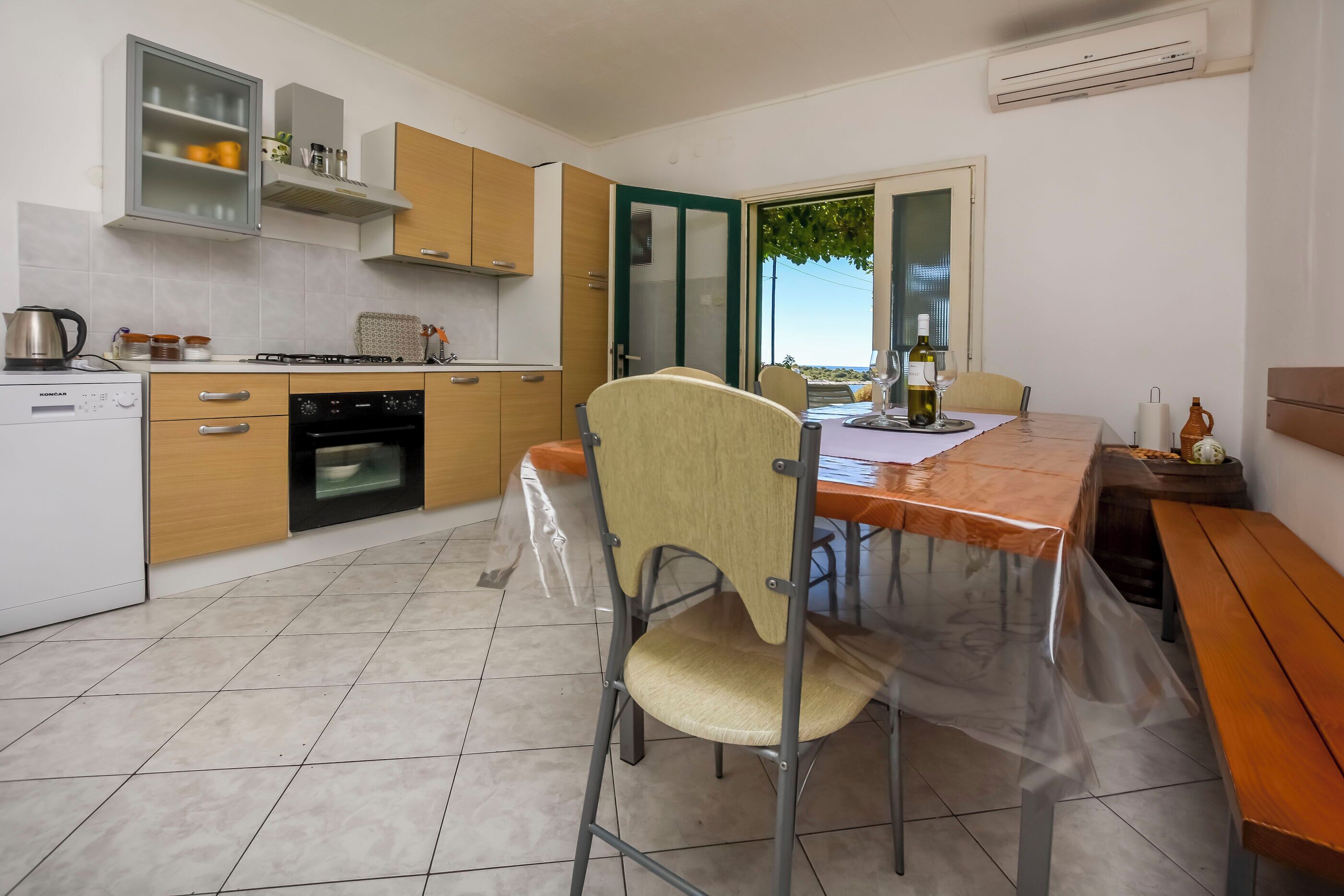 A modern kitchen with a dining area, featuring a foldable table, chairs, and a view through a glass door.
