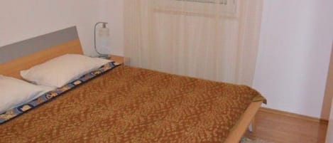 Un dormitorio con cama, una ventana con persianas, una mesita de noche y una alfombra.