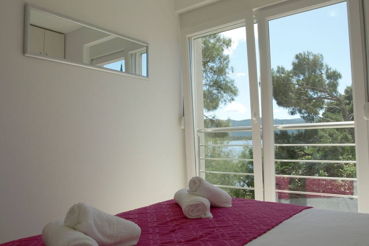 A bedroom with a bed, a window with a view of trees and mountains, and a mirror on the wall.