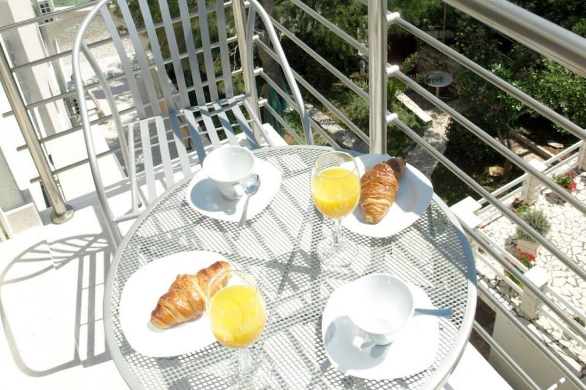 A balcony with a table set for breakfast, overlooking a body of water and a small island.