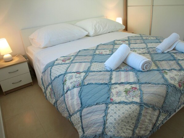 A neatly made bed with a quilt, two rolled towels, and a bedside lamp on a nightstand. - Apartment At the sea (Slivno)