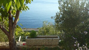 A garden with a view of the sea, a stone planter, and a tree. - Apartments Mirela (Omis)