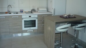 A modern kitchen with a built-in oven, a stainless steel range hood, a white refrigerator, and a bar area with stools. - Apartments Mirela (Omis)
