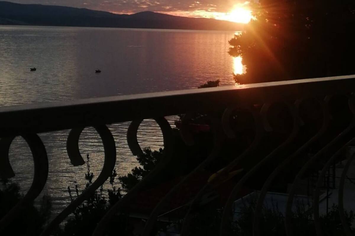 A sunset over a calm lake with boats, a railing in the foreground, and distant mountains.