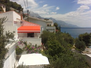A coastal building with a balcony overlooking the sea, surrounded by greenery and mountains. - Apartments Mirela (Omis)