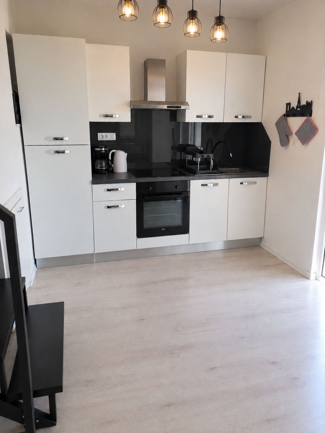 A modern kitchen with white cabinets, a black countertop, and a built-in oven. There are three pendant lights above the sink.