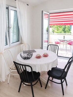 A round table with a white tablecloth, four chairs, two cups with saucers, and a bottle of champagne. - Apartments Mirela (Omis)