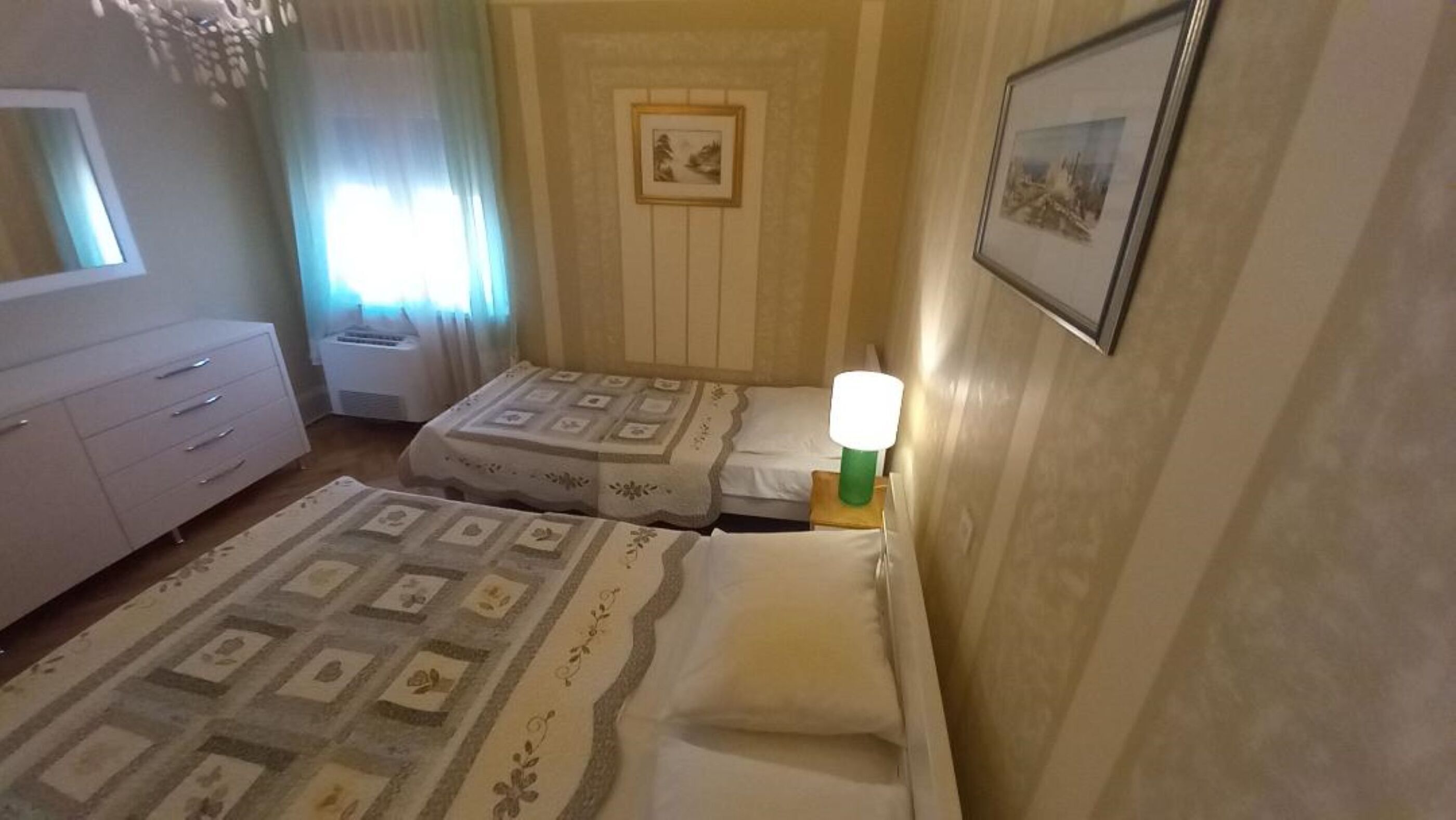 A hotel room with two beds, a dresser, a window with curtains, and a framed picture on the wall.