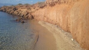 Ein Küstenstrand mit klarem, flachen Wasser, felsigen Klippen und spärlicher Vegetation.
