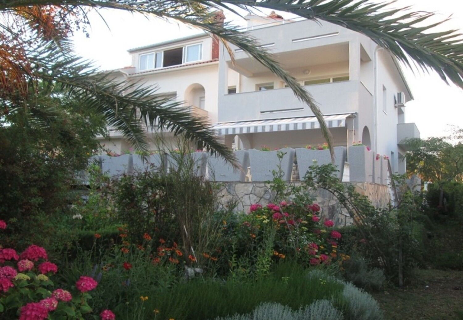Um edifício com várias andares e varandas, rodeado por vegetação exuberante e plantas floridas.