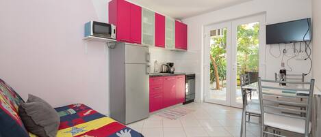 A compact living space with a kitchenette, a dining area, and a bed with a colorful quilt.