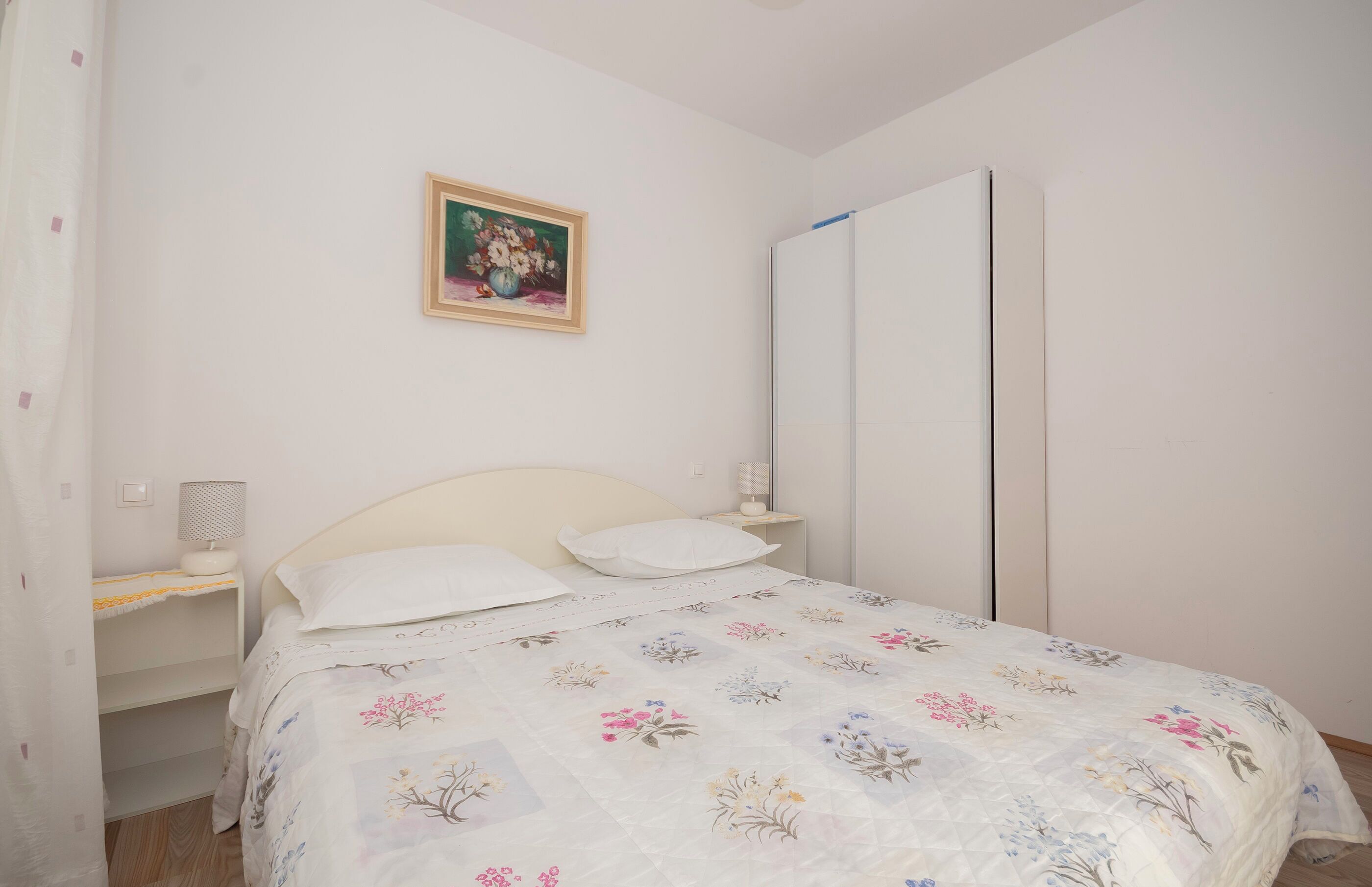 Una camera da letto con un letto, un comodino, una lampada, un armadio e un quadro appeso al muro.