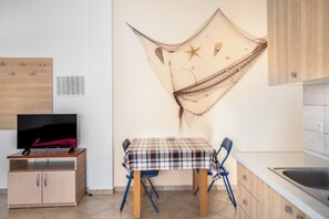 Eine kleine Küche mit einem Holzkasten, einem Tisch mit kariertem Tischläufer und einem Fernseher auf einem Holzständer.