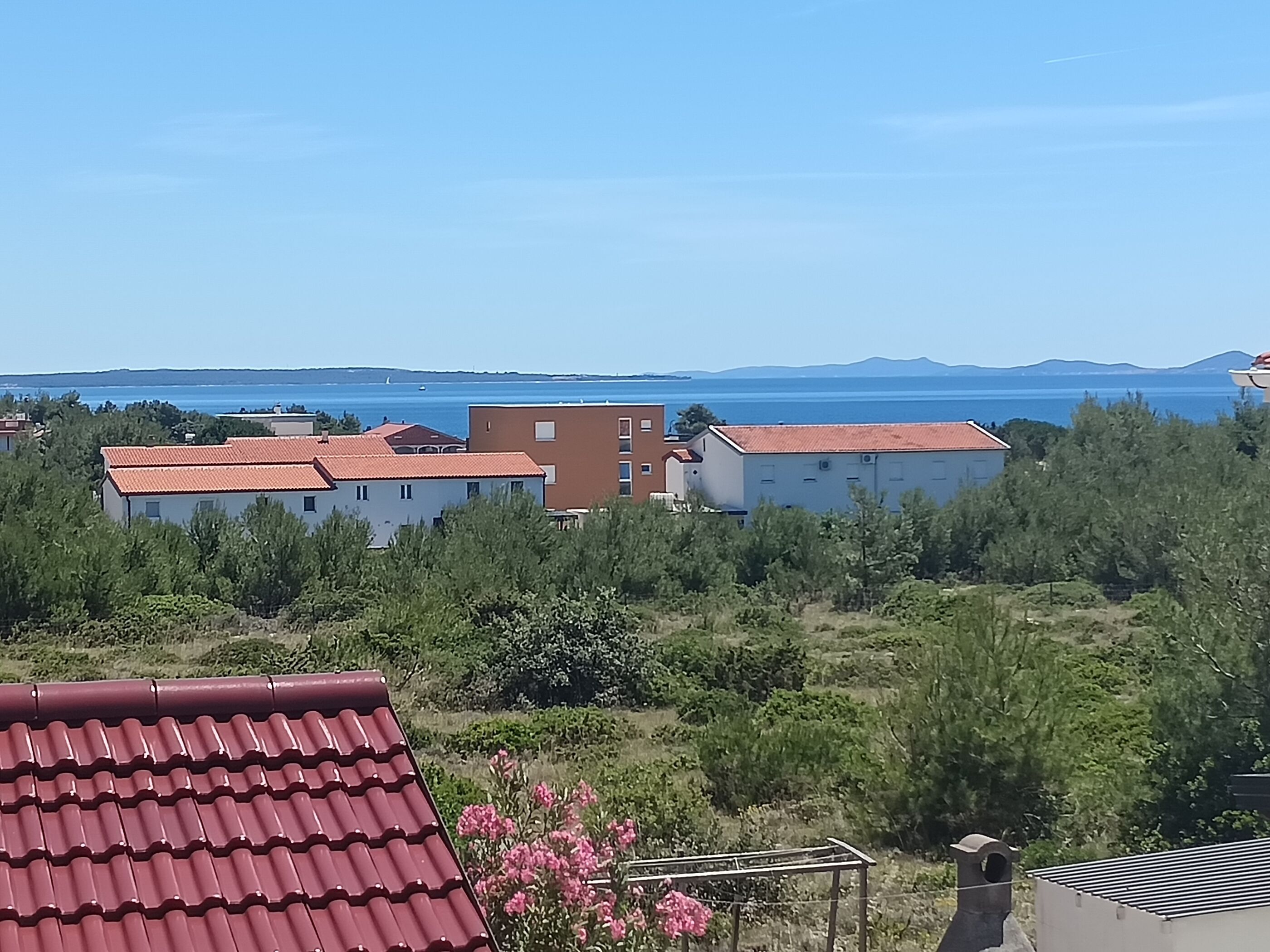 A residential area with buildings, a clear sky, and a view of the sea.