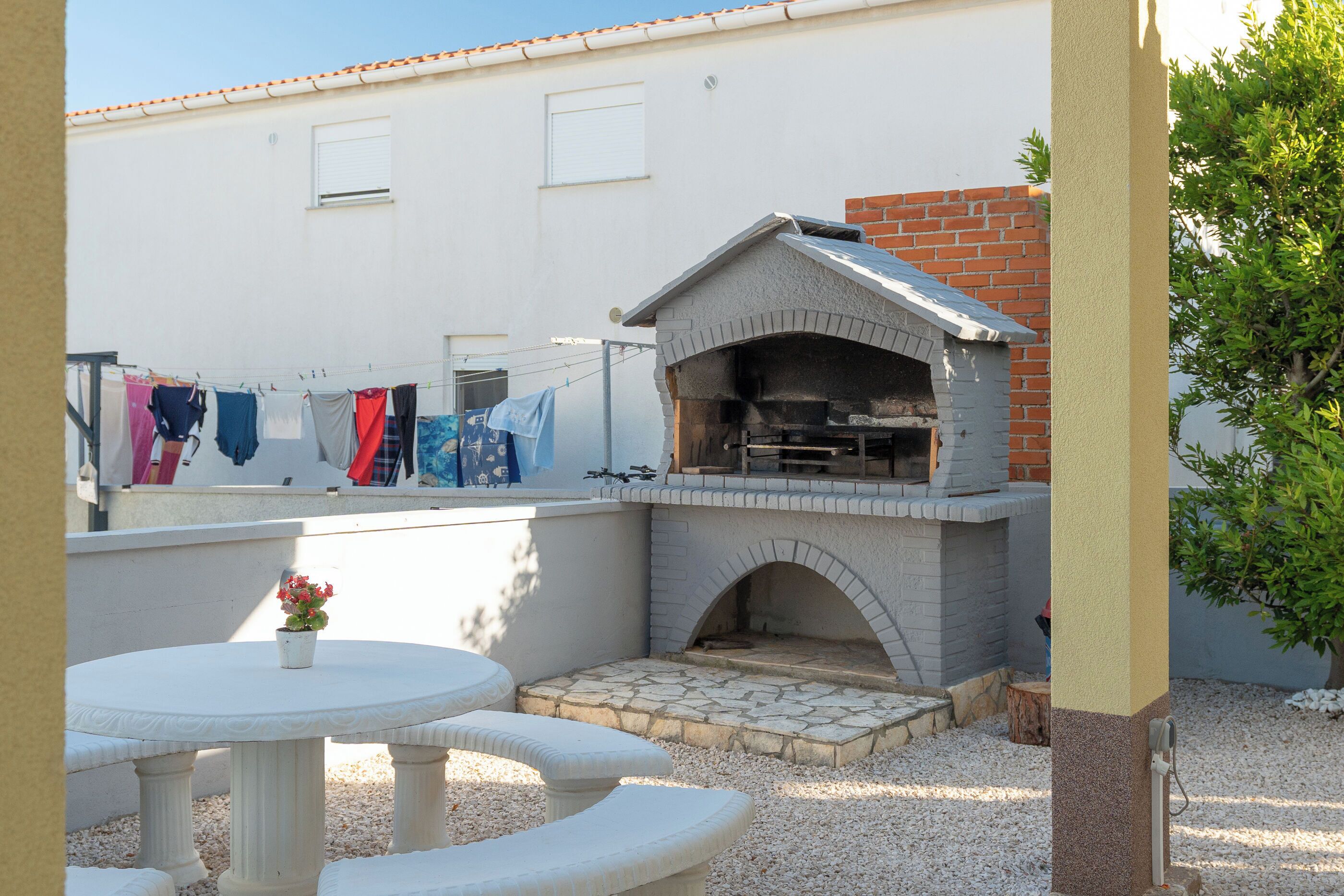 A patio with a brick oven, a white table with chairs, and a clothesline with laundry.