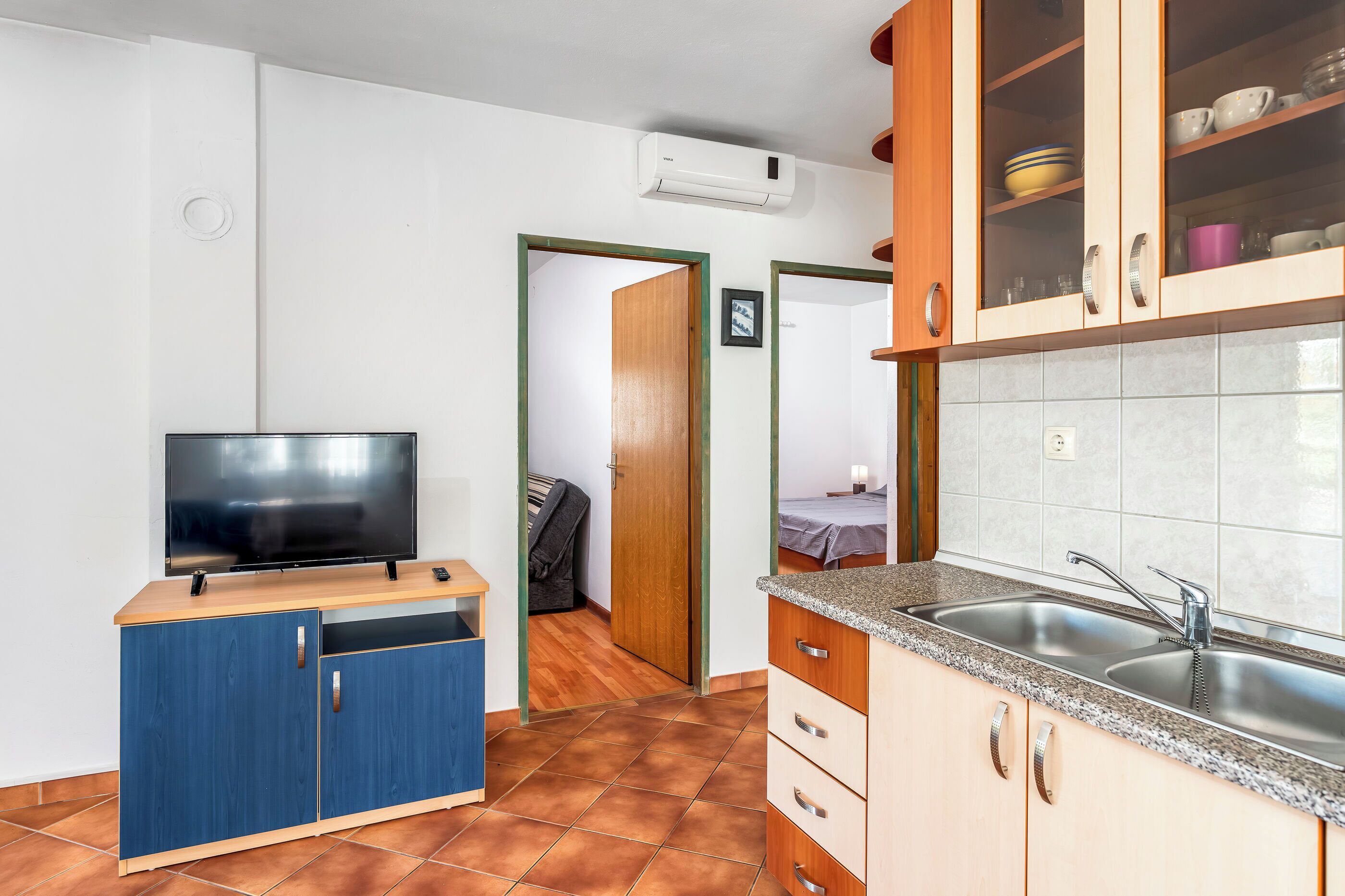 Een kleine keuken met een televisie, kastjes en een spoelbak.