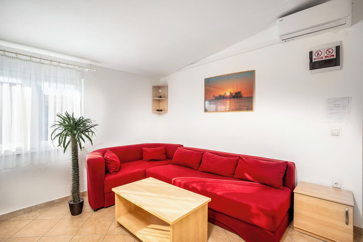 Ein rotes Ecksofa, ein Couchtisch aus Holz, ein Blumentopf, ein kleiner Nachttisch aus Holz und ein Gemälde an der Wand.