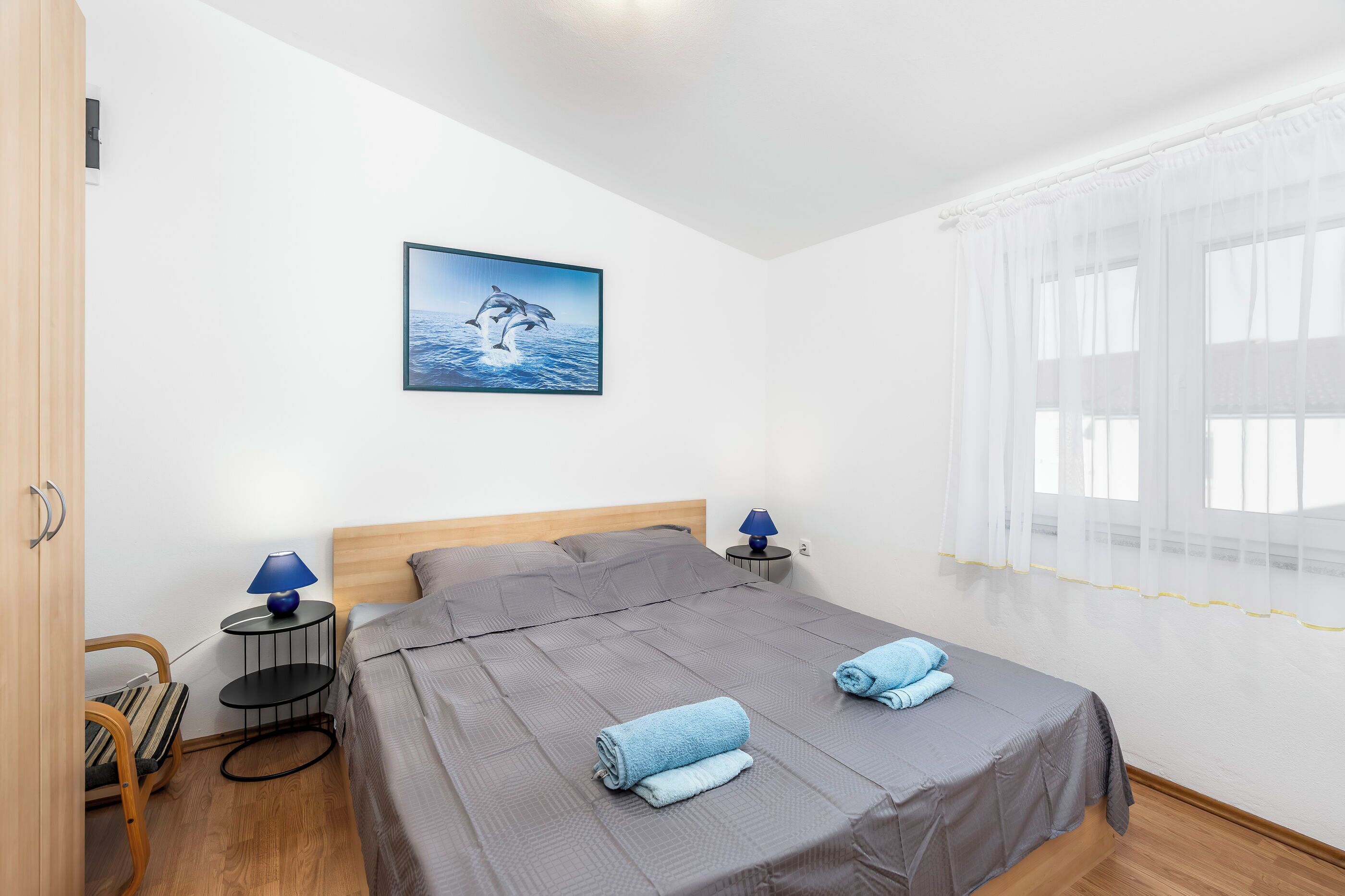 A neatly arranged bedroom with a bed, two bedside tables with lamps, a chair, and a picture on the wall.