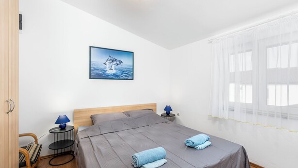 A neatly arranged bedroom with a bed, two bedside tables with lamps, a chair, and a picture on the wall. - Apartment Draga (Vir)