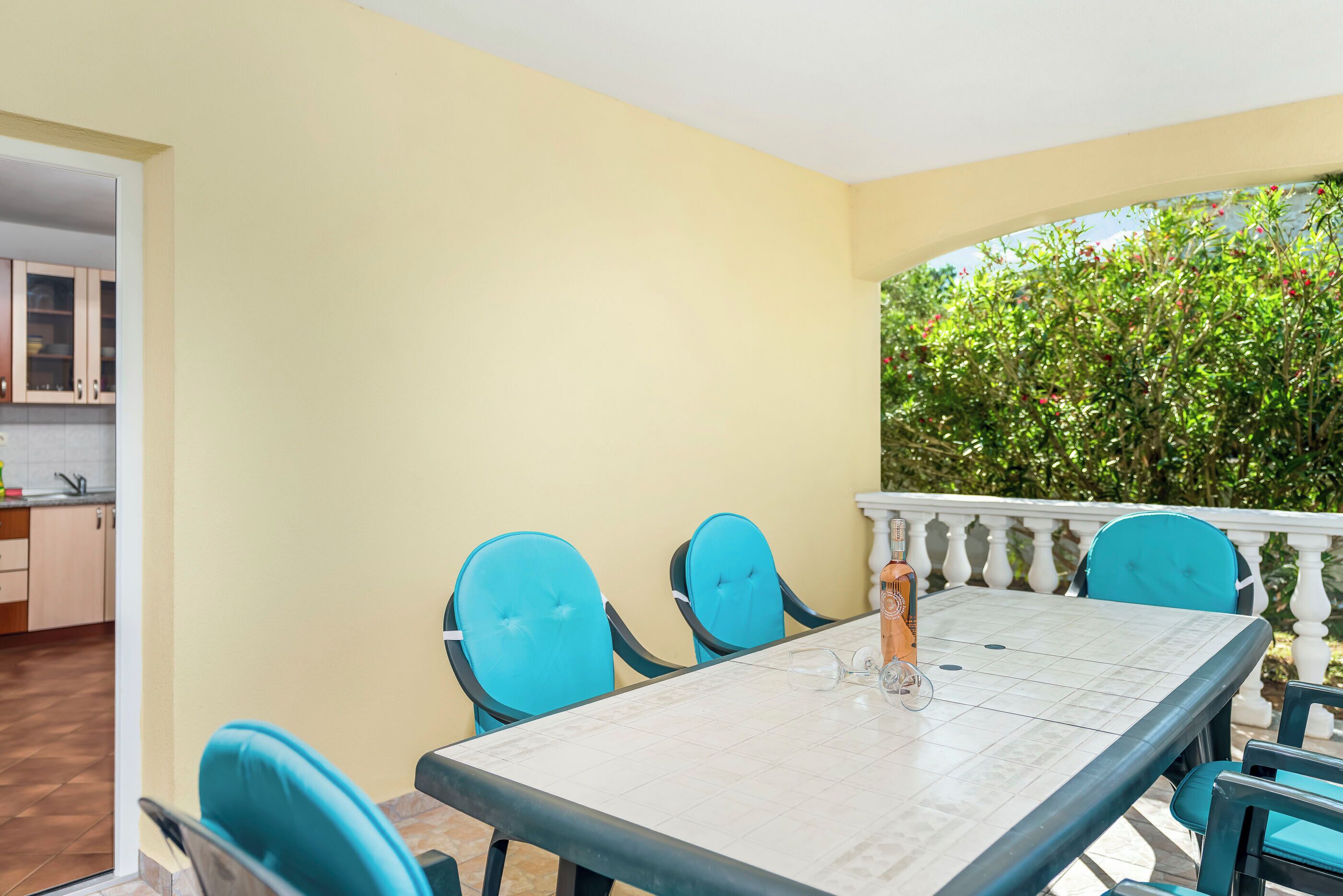 Un coin repas avec une table blanche et des chaises bleues, un verre de jus d’orange et une vue sur la verdure.