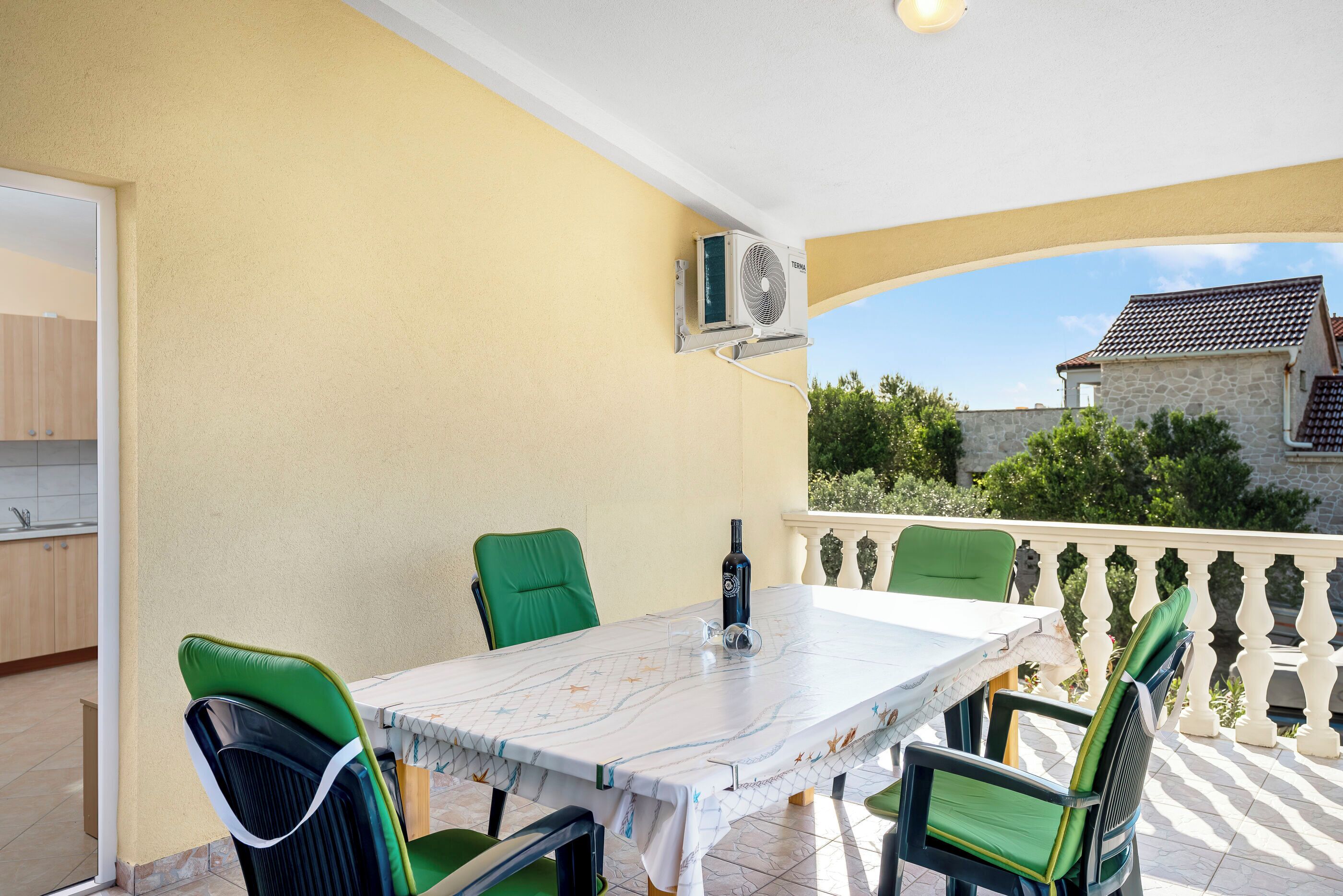 A balcony with a table and chairs, an air conditioning unit, and a view of a stone building.