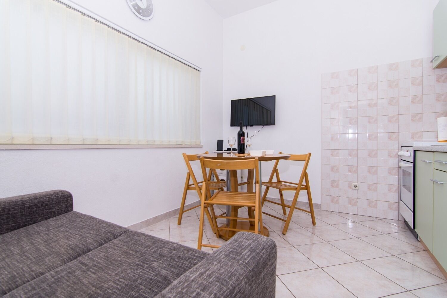 A compact living space with a dining area, a sofa, a TV mounted on the wall, and a kitchen area.