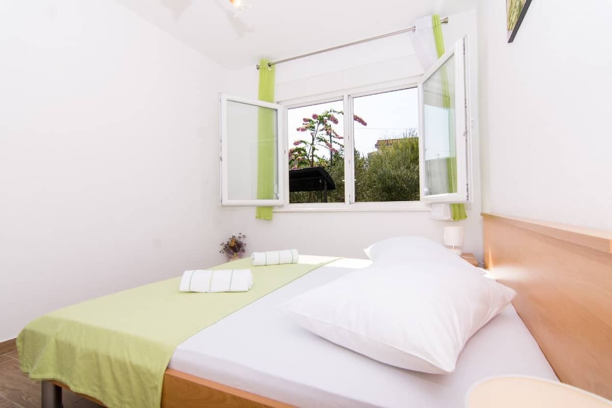 A bedroom with a bed, a window with green curtains, a bedside table, and a small plant.