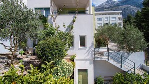 Un edificio moderno con balcón, rodeado de vegetación y una montaña al fondo.