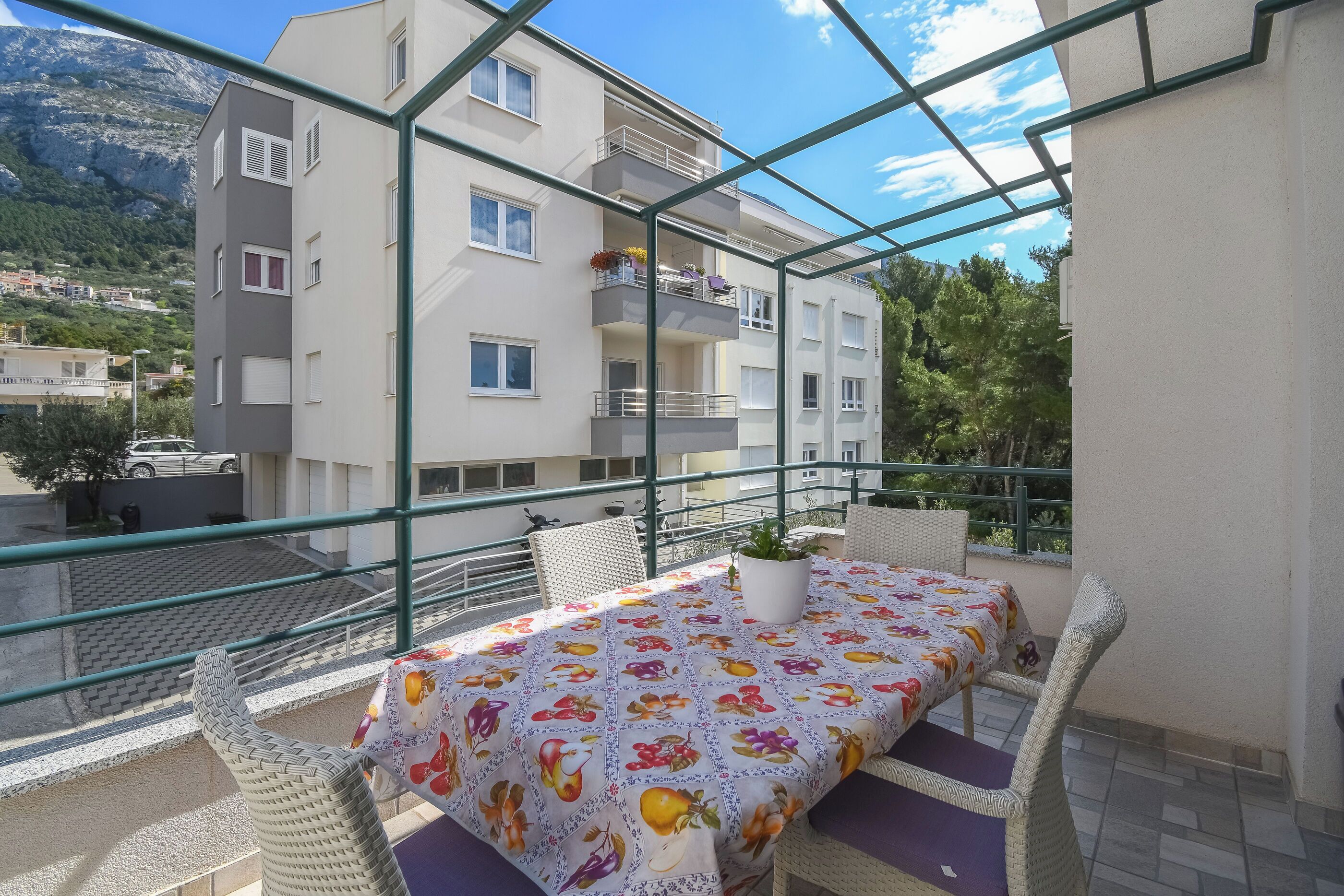 En balkon med et bord og stole, en potteplante og udsigt til en bygning og bjerge.