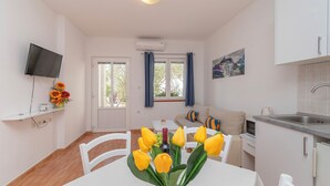 Una cocina moderna con un lavamanos, estufa y microondas. Hay una zona de comedor con una mesa y sillas, y un televisor montado en la pared.
