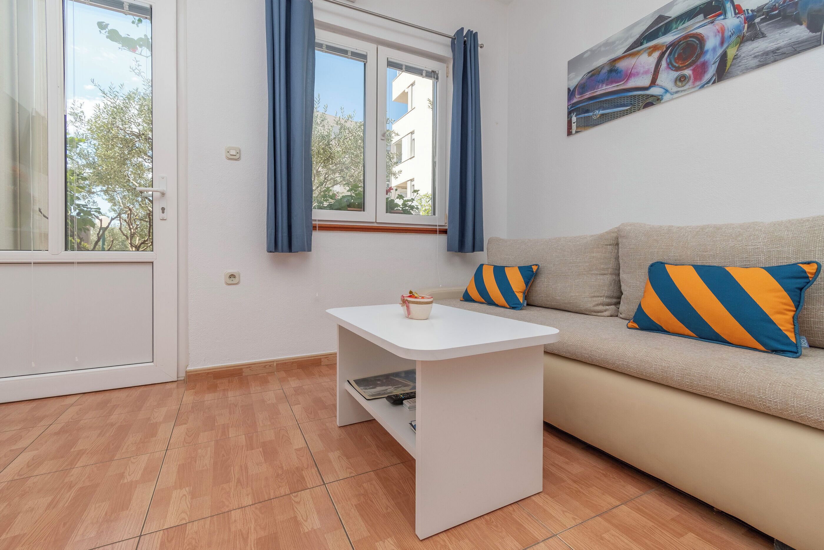 Uma sala de estar com sofá, uma mesinha branca e uma janela com cortinas.